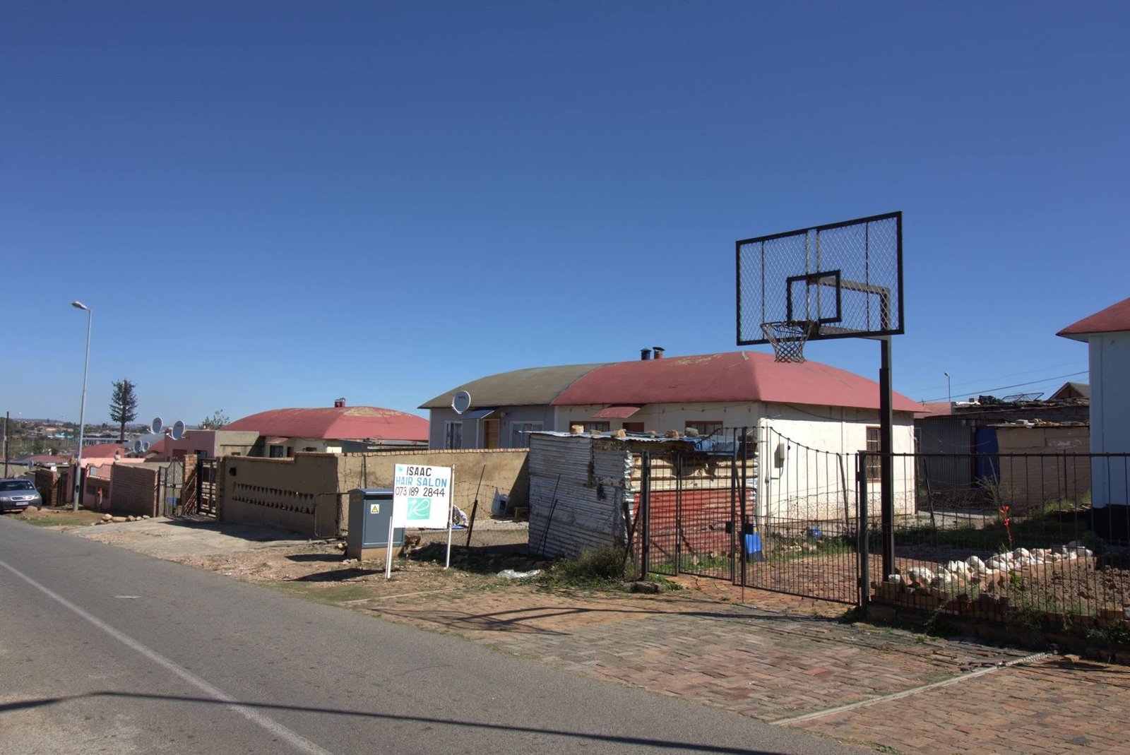 Township tour Soweto: straat met huizen met rode daken, een bord van Isaac Hair Salon en een basketbalpaal onder een strakblauwe lucht