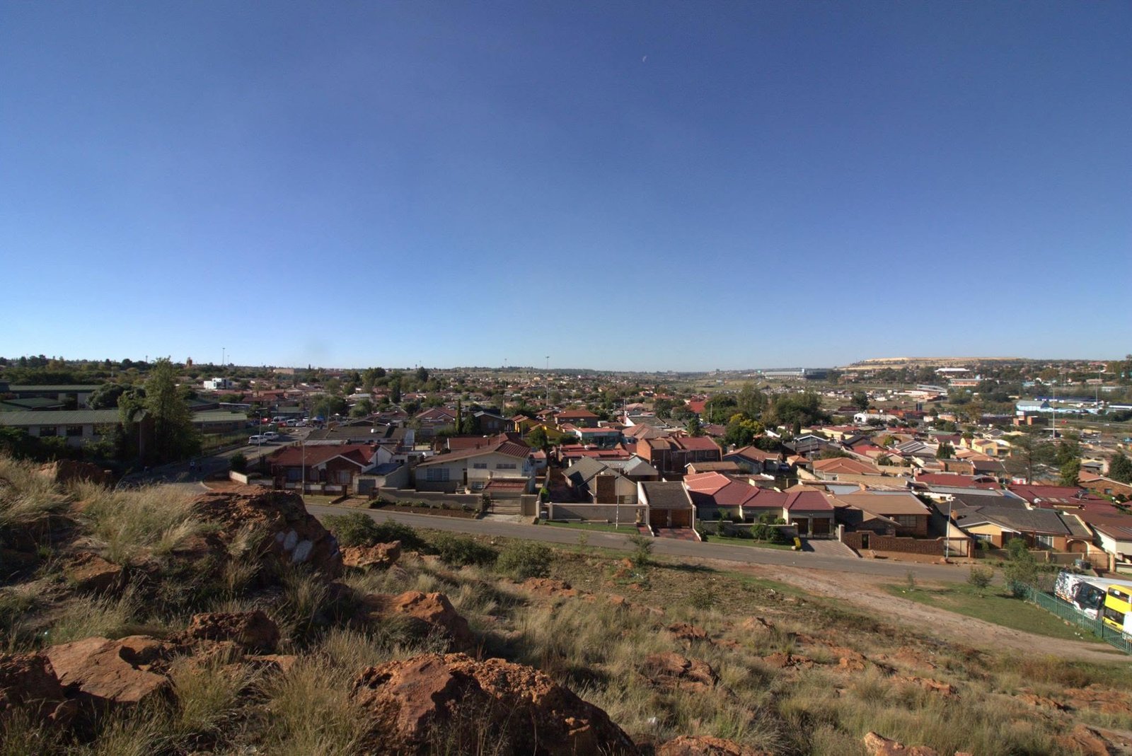 Township tour Zuid-Afrika: uitzicht vanaf een rotsige heuvel over de huizen en straten van Soweto onder een strakblauwe lucht